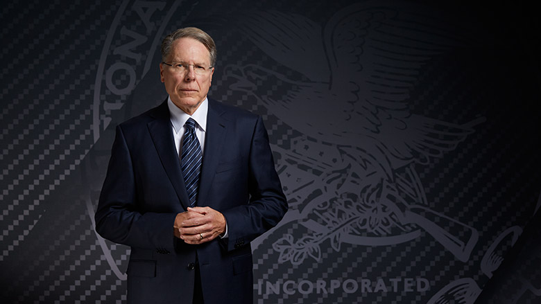 Wayne LaPierre in a dark suit standing in front of the NRA emblem