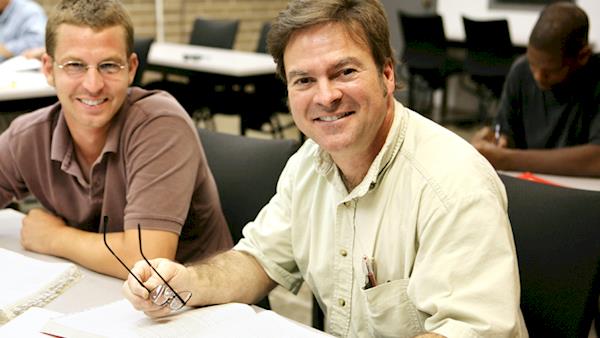 Two men smiling in a Classroom with other students