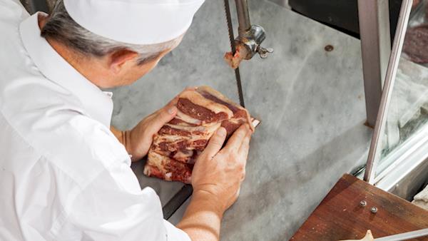 Professional Butcher Slicing Meat with a Saw