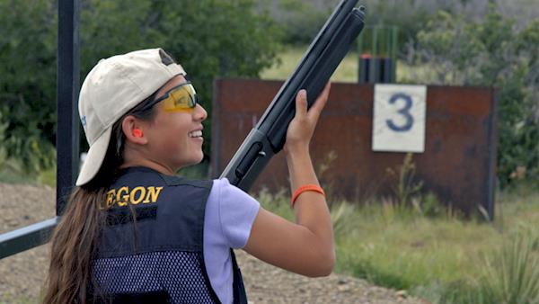 Young girl smiles after shooting a shotgun on a range.