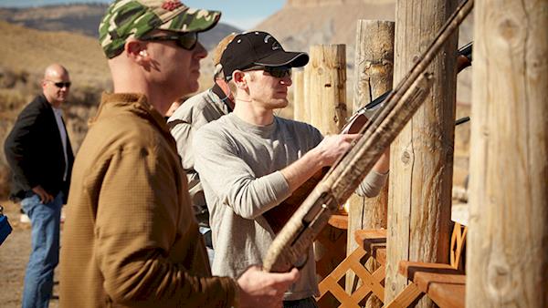 Several men in ball caps shooting shotguns at an outdoor range.