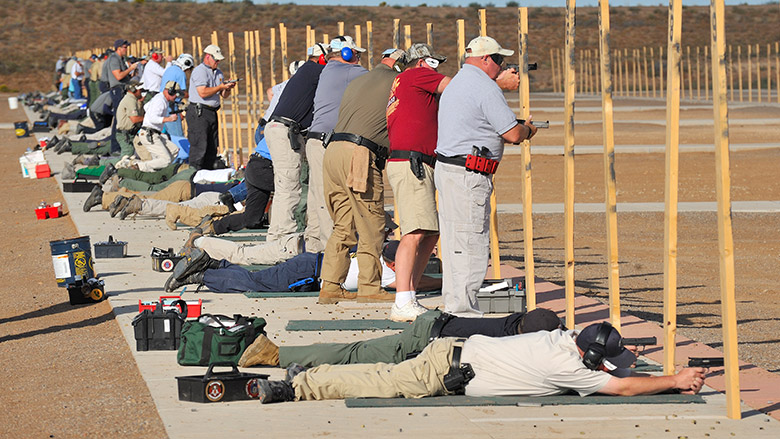 NRA Competition firing line with shooters laying prone and standing while they shoot pistols.